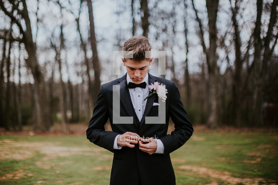 teen boy buttoning a tuxedo 