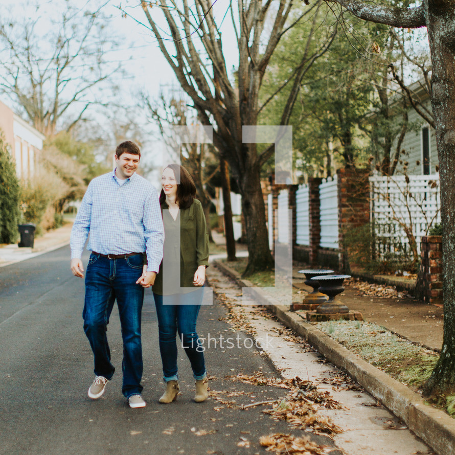 couple holding hands walking down a neighborhood street 