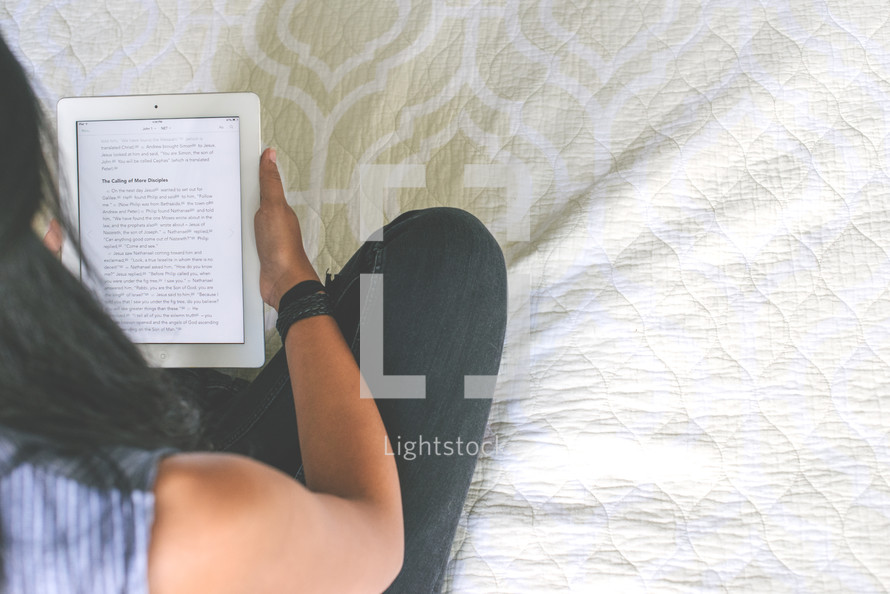 young woman reading a Bible on a a tablet in bed 