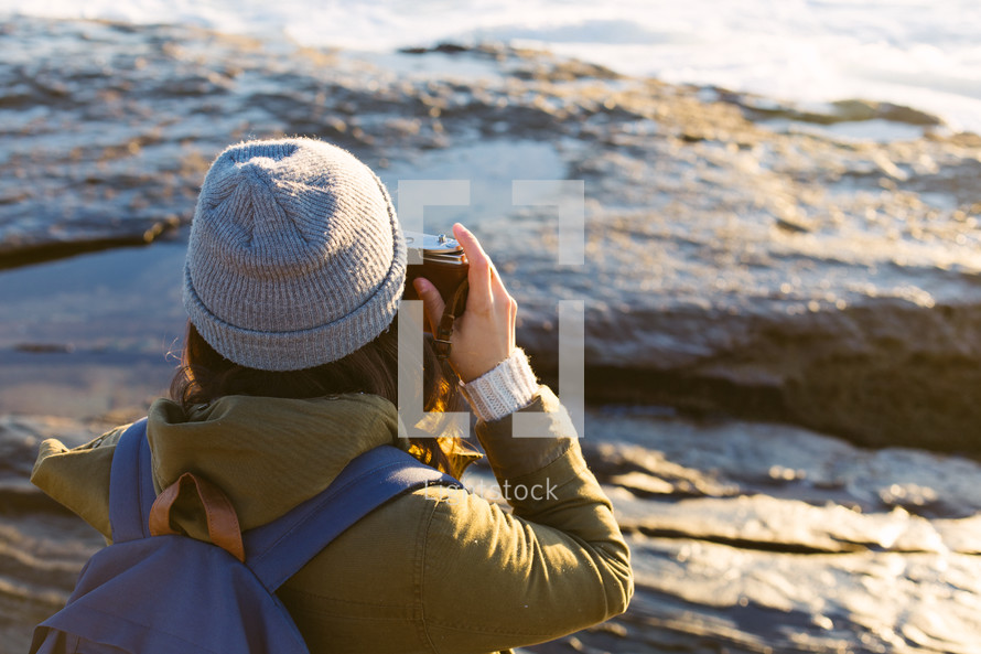 woman standing on rock on the beach taking pictures with a camera 