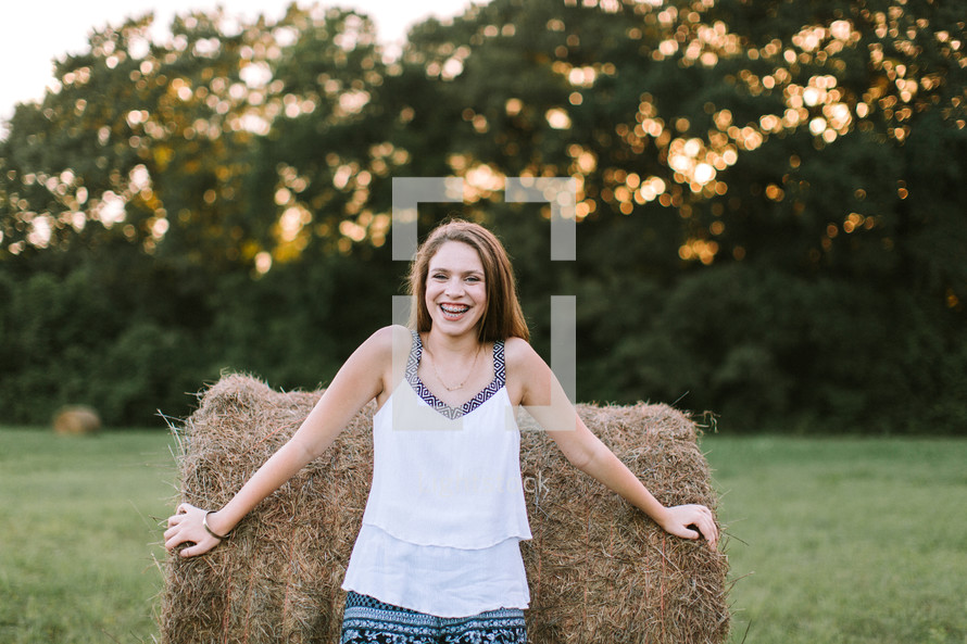 teen girl standing in front of a hay bale smiling