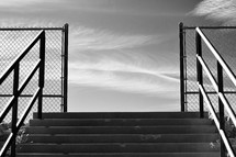outdoor steps leading to a basketball court and wispy clouds in the sky in black and white 