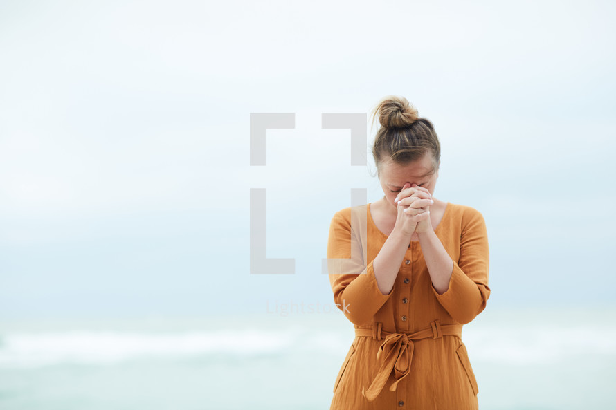 a woman standing on a beach praying
