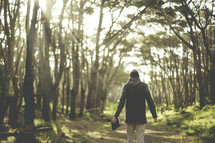 a man walking on a path in a forest carrying a Bible 