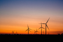 silhouettes of wind turbines at sunset 