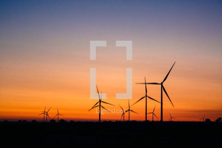 silhouettes of wind turbines at sunset 