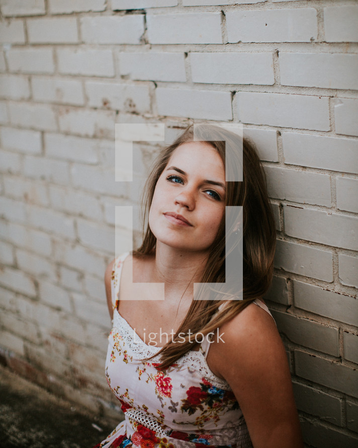 teen girl sitting in front of a white brick wall 