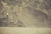 man standing on a beach near a cliff 