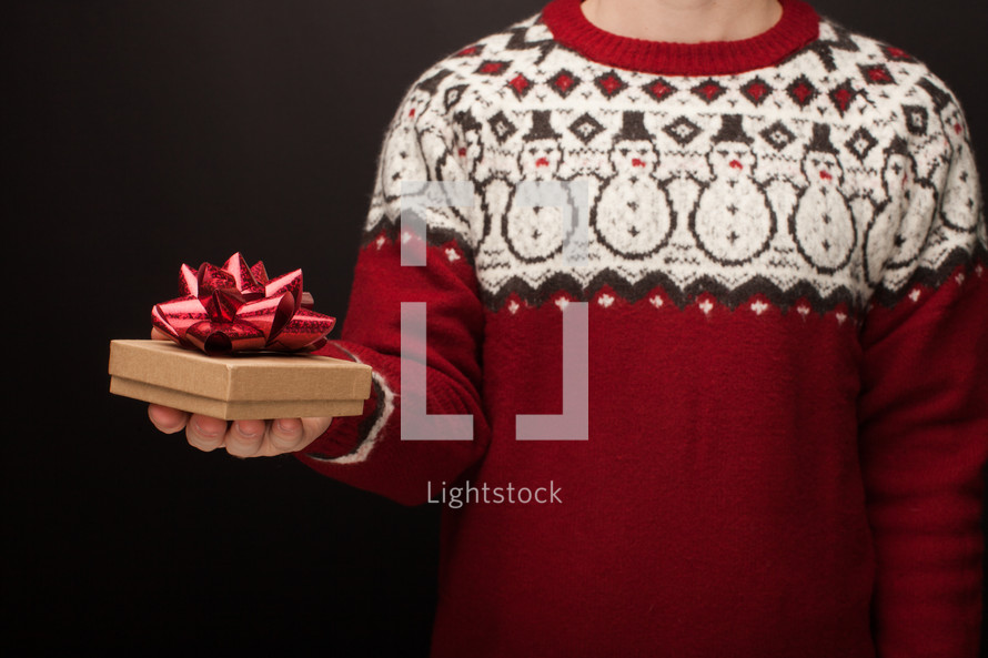 a man in a Christmas sweater holding a gift box 