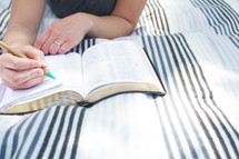 a woman reading a Bible and writing in a journal 