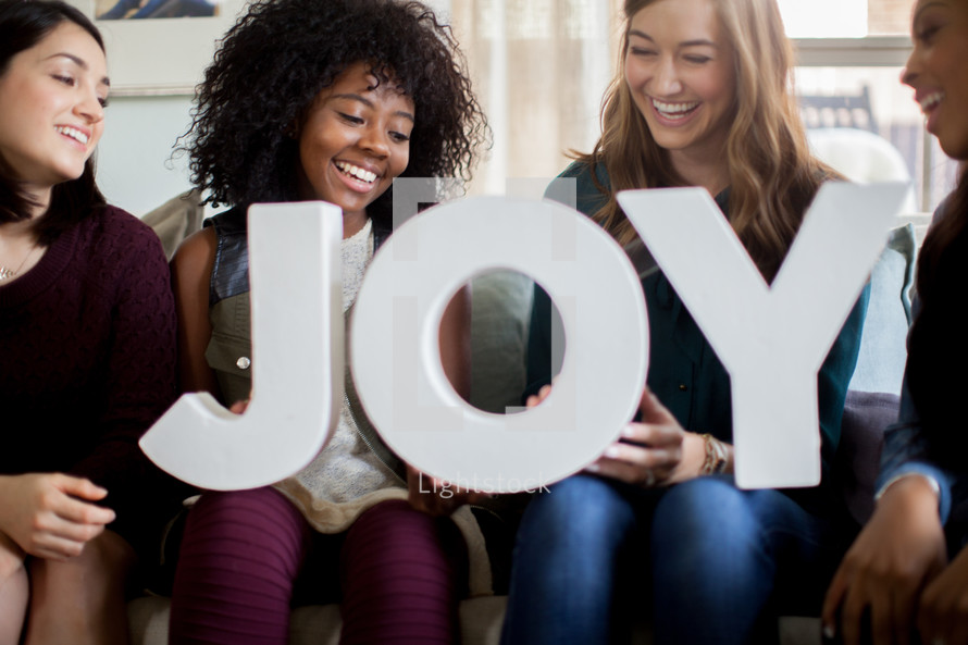 Four women smiling and holding letters spelling "joy."