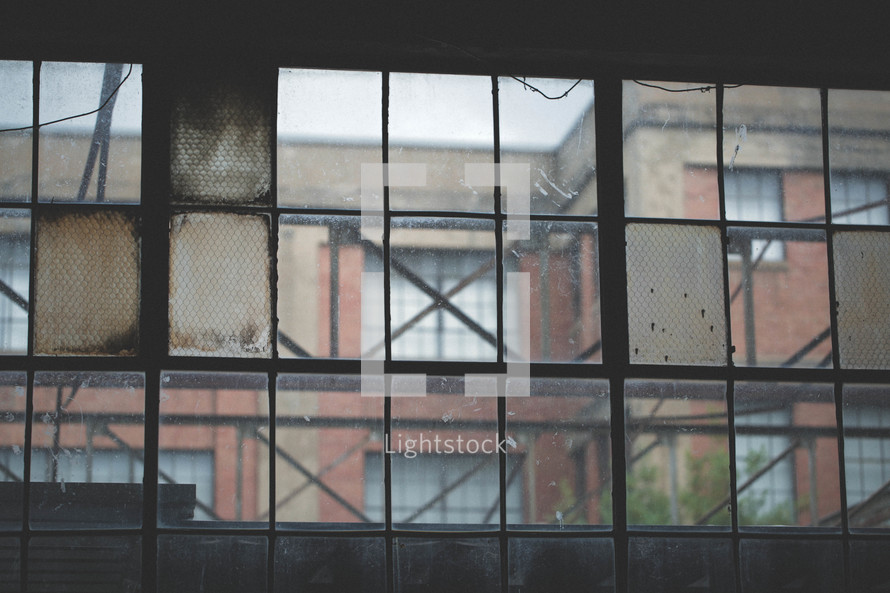 Brick industrial buildings seen through a bank of windows.