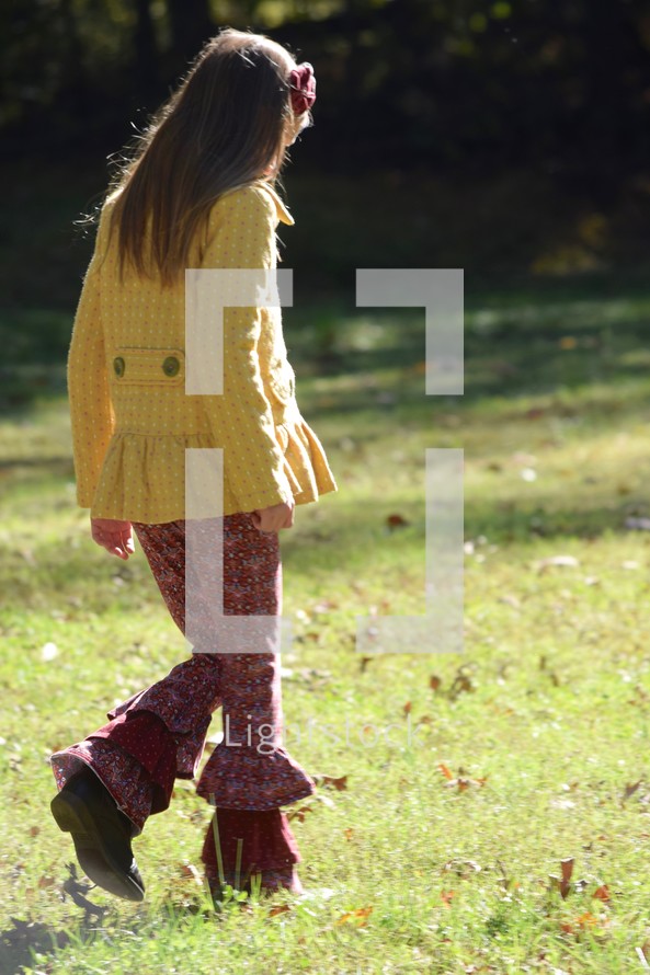 a girl walking through the grass in fall 
