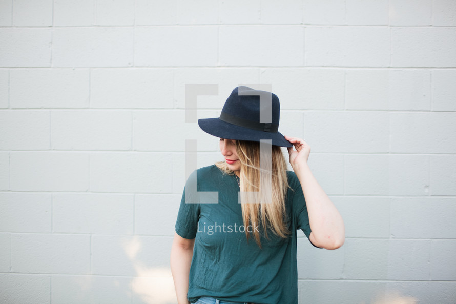 woman in a hat standing in front of a white wall 