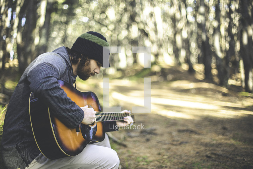 a man playing a guitar in a forest 