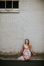 teen girl sitting on a sidewalk in front of a white wall 