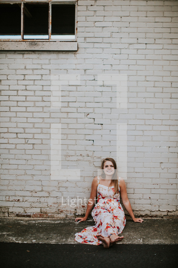 teen girl sitting on a sidewalk in front of a white wall 