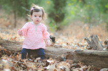 toddler girl sitting on a fallen tree in fall leaves 