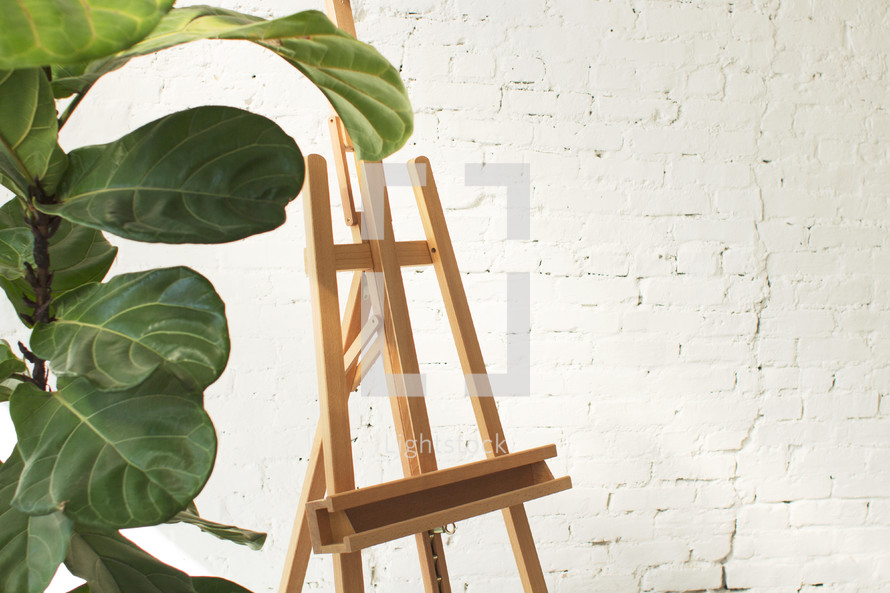 A green potted plant next to an empty wooden easel.