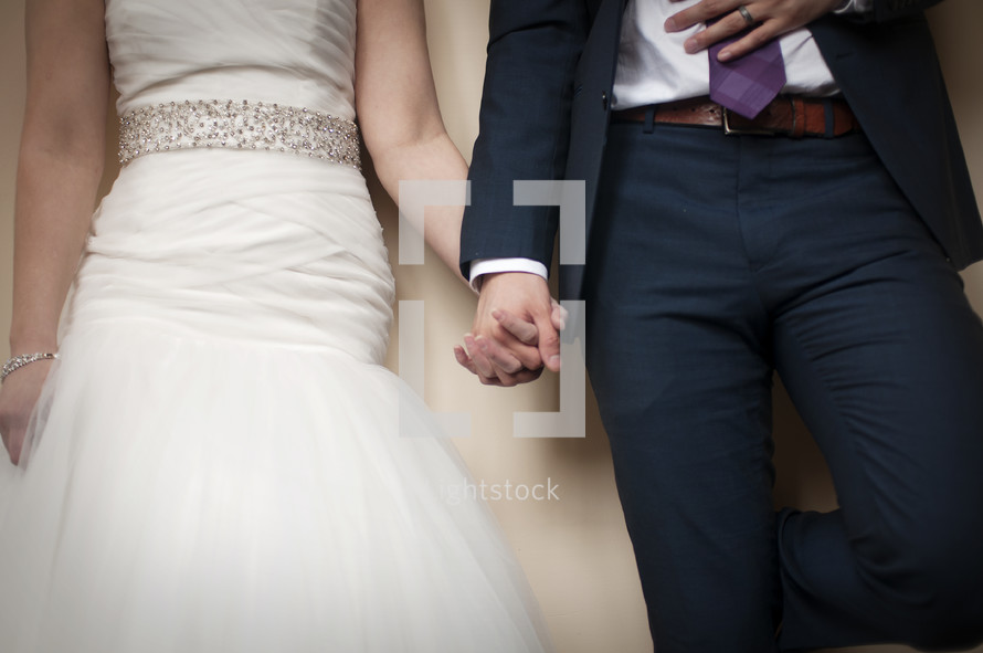 torso of bride and groom holding hands 