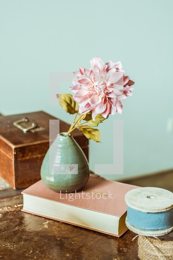 flower in a vase, book, and spools of ribbon on a table 