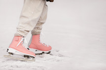 Cropped photo of child girl legs wearing in pink skates and warm clothes at the rink on natural ice on cold winter day. Child ice skating on frozen lake with in the snowy forest. Happy holiday