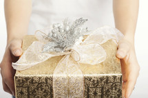 Hands holding out a gold and silver wrapped gift box