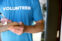 A man writing with a pen on a clipboard while wearing a t-shirt saying, "volunteer."
