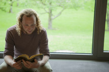 a man sitting in a window reading a Bible 