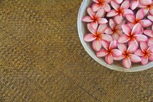 Bowl of pink tropical flowers on a woven mat