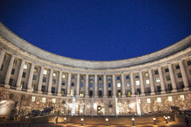In side view of a coliseum, a large number of columns, and lighted trees