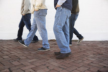 Group of men walking down a sidewalk. 