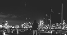 A man standing and looking at the city skyline at night.