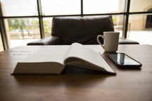 open Bible, cellphone, and coffee mug on a table 