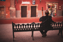 a man with a guitar sitting on a bench 
