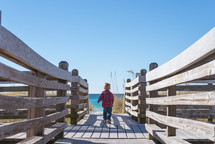 a toddler boy walking on a boardwalk 