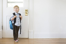 boy child with a book bag standing at a door - first day of school 