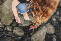 a girl finds colourful starfish among the rocks