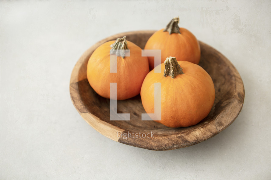 Three small pumpkins in a wooden bowl