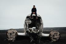 a man sitting on a wreckage of an airplane crash site 