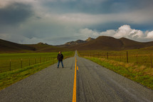 man standing in the middle of a rural road 