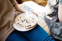 A woman sitting with a blueberry bagel on a white plate.