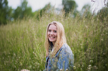 a smiling young woman standing in a field of tall grasses 