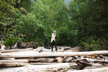 a woman walking over driftwood on a shore 