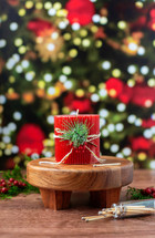 Red Christmas Candle with Greenery and Berries with Christmas Tree and Lights in the Background