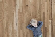 A toddler boy lying on a wood floor with his eyes closed. 