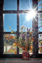 Pitcher full of flowers in sunlit window