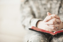 Female soldier in uniform praying over an open Bible.