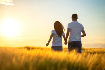 couple standing in a golden field holding hands 