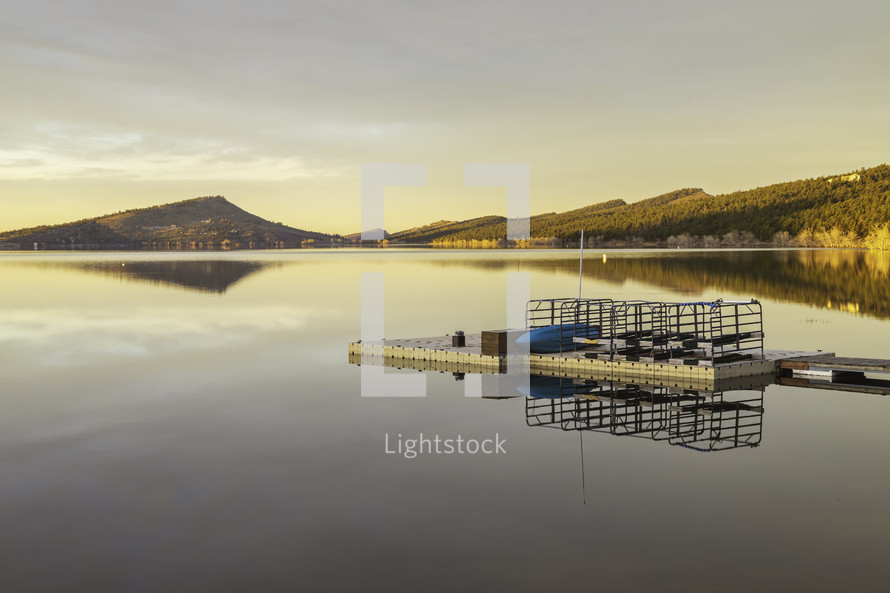 The sun hits the hillside on the mountain lake at sunrise. The boating dock reflects in Carter Lake located in Loveland Colorado
